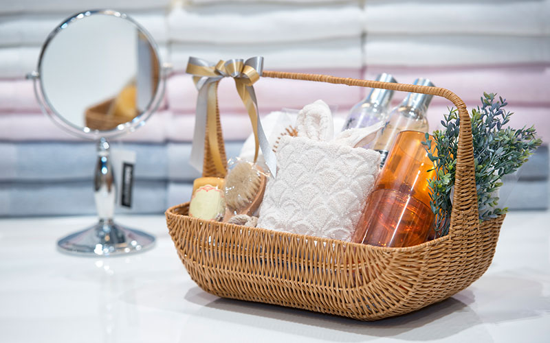 a basket containing bottles of amber lotion, a face towel, a brush. and other personal care items.