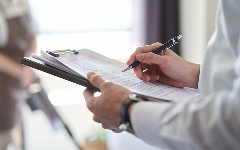 close up of hands holding a clip board and checking off a list with a soft focus cleaner in the background
