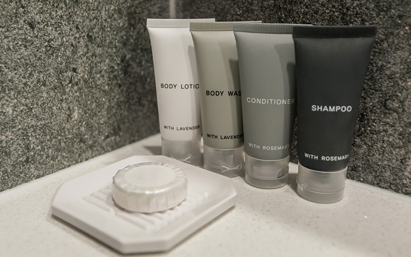 Arow of tubes of lotion, shampoo and conditioner, and a bar of soap